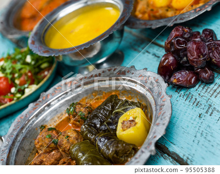 Eid Mubarak Traditional Ramadan Iftar dinner. Assorted tasty food in authentic rustic dishes on wooden blue background. Turkish Bosnian food meat kebab, pita, Sarma, klepe, sogan dolma. Eid Mubarak Traditional Ramadan Iftar dinner. Assorted tasty food in authentic rustic dishes on wooden blue background. Turkish Bosnian food meat kebab, pita, Sarma, klepe, sogan dolma. 95505388