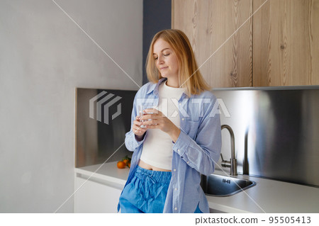 Beautiful young woman drinking pure fresh water from transparent glass in kitchen 95505413