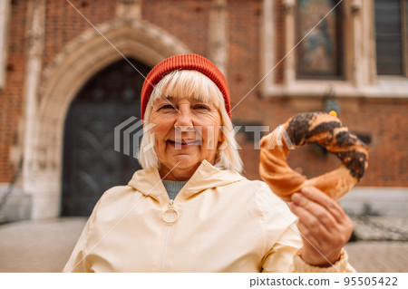 Senior woman holding prezel, traditional polish snack on the Market square in Krakow Senior woman holding prezel, traditional polish snack on the Market square in Krakow 95505422