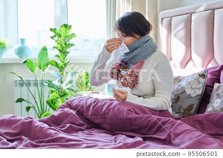 Sick woman holding handkerchief, sneezing, wiping her nose, sitting in bed at home Sick woman holding handkerchief, sneezing, wiping her nose, sitting in bed at home 95506501