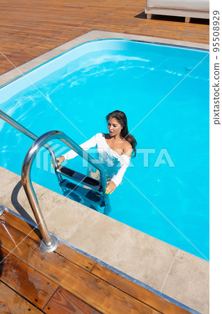 Confident alluring lady standing on stairs in pool during summer vacation 95508929