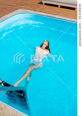 Sensual lady in wet dress standing in pool during summer vacation Sensual lady in wet dress standing in pool during summer vacation 95508930