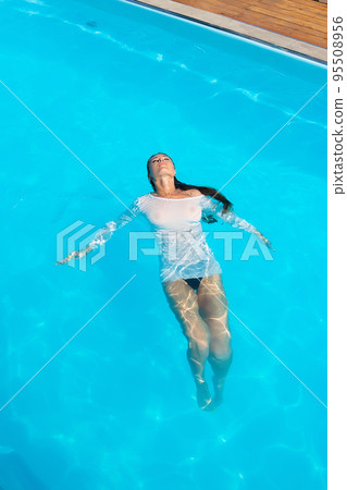 Sensual lady in wet dress standing in pool during summer vacation Sensual lady in wet dress standing in pool during summer vacation 95508956