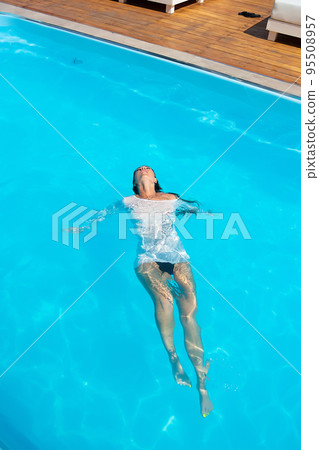 Sensual lady in wet dress standing in pool during summer vacation Sensual lady in wet dress standing in pool during summer vacation 95508957