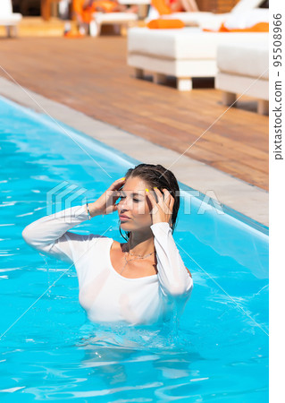 Sensual lady in wet dress standing in pool during summer vacation Sensual lady in wet dress standing in pool during summer vacation 95508966