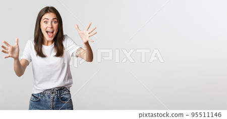 Excited brunette girl smiling amazed and raising hands to catch something 95511146