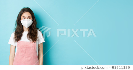Covid-19, vaccination and quarantine concept. Cheerful female student wearing respirator to prevent catching coronavirus, social distancing during global pandemic, blue background 95511329