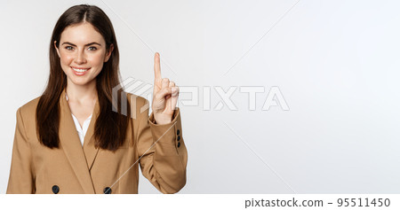 Portrait of corporate woman, saleswoman showing number one finger and smiling, standing in suit over white background Portrait of corporate woman, saleswoman showing number one finger and smiling, standing in suit over white background 95511450