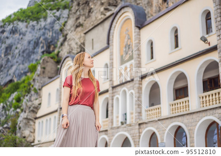Woman tourist in Monastery of Ostrog, Serbian Orthodox Church situated against a vertical background, high up in the large rock of Ostroska Greda, Montenegro. Dedicated to Saint Basil of Ostrog 95512810