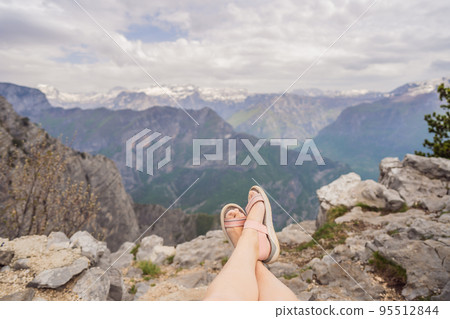 Woman tourist on background of Breathtaking panoramic view of the Grlo Sokolovo gorge in Montenegro. In the foreground is a mountain, the flat side of which forms a cliff, and the ridge is overgrown Woman tourist on background of Breathtaking panoramic view of the Grlo Sokolovo gorge in Montenegro. In the foreground is a mountain, the flat side of which forms a cliff, and the ridge is overgrown 95512844