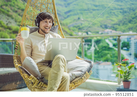 Handsome caucasian man sitting on the terrace working from home using computer laptop. Young man teaches a foreign language or learns a foreign language on the Internet on his balcony. Online language Handsome caucasian man sitting on the terrace working from home using computer laptop. Young man teaches a foreign language or learns a foreign language on the Internet on his balcony. Online language 95512851