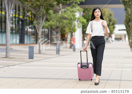 A businesswoman walking with a backpack and a suitcase 95513179