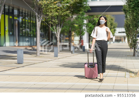 A business woman wearing a mask, carrying a backpack, and walking with a suitcase 95513356