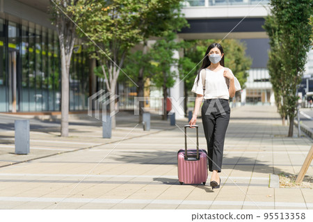 A business woman wearing a mask, carrying a backpack, and walking with a suitcase 95513358