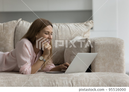 Pretty woman lying on sofa using laptop at cozy home 95516000