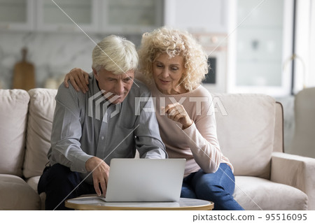 Couple sit on couch staring at laptop using ecommerce website Couple sit on couch staring at laptop using ecommerce website 95516095
