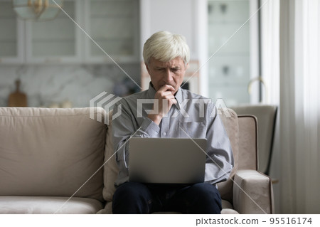 Frown older man sit on sofa with laptop Frown older man sit on sofa with laptop 95516174