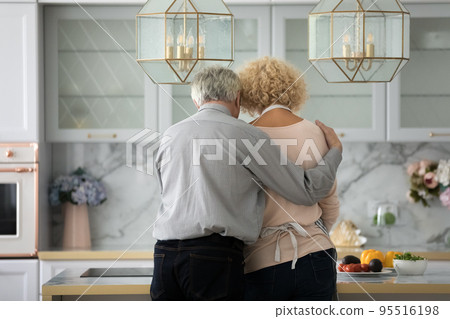 Rearview loving older husband hugging wife preparing breakfast in kitchen Rearview loving older husband hugging wife preparing breakfast in kitchen 95516198