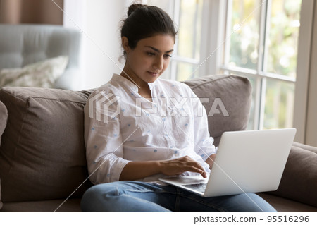 Attractive focused Indian woman using laptop at home 95516296