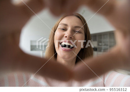 Happy woman showing symbol of love, smile staring at camera 95516312