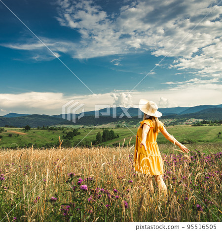 Woman in yellow dress and hat staying at the green meadow in the mountain 95516505