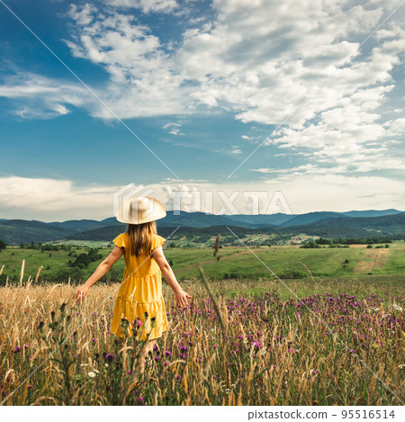 Woman in yellow dress and hat staying at the green meadow in the mountain 95516514