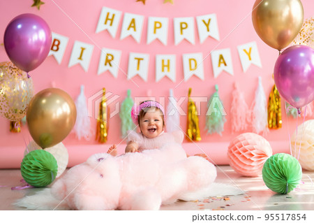 Laughing little girl sits near paper balls with teddy in holiday dress on pink birthday background Laughing little girl sits near paper balls with teddy in holiday dress on pink birthday background 95517854