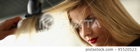 Hairdresser using hairdryer tool to dry clients lock of hair 95520523