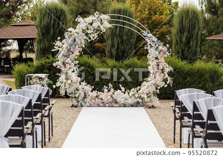 Wedding ceremony. Very beautiful and stylish wedding arch, decorated with various fresh flowers, standing in the garden. Wedding ceremony. Very beautiful and stylish wedding arch, decorated with various fresh flowers, standing in the garden. 95520872