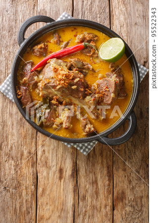 Spicy goat curry with coconut milk and spices close-up in a pan on the table. Vertical top view 95522343