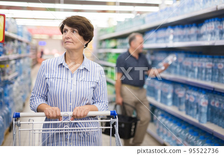 Mature woman considering bottle of vermouth in supermarket Mature woman considering bottle of vermouth in supermarket 95522736