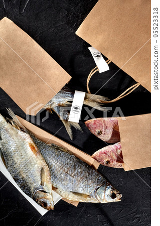 Salted air-dried roach and surmullets in kraft paper packets on black background Salted air-dried roach and surmullets in kraft paper packets on black background 95523318