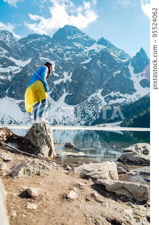 A woman with Ukrainian flag is standing on the shore of a lake. Morskie Oko 95524062