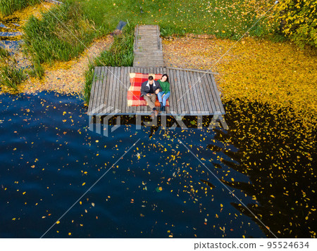 couple laying on the pier at the lake covered with autumn leaves couple laying on the pier at the lake covered with autumn leaves 95524634