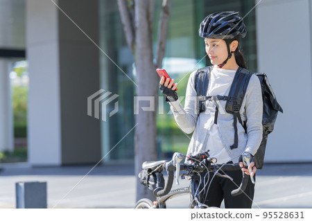 A food delivery woman pulling a road bike with a smartphone in her hand A food delivery woman pulling a road bike with a smartphone in her hand 95528631