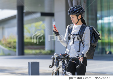 A food delivery woman pulling a road bike with a smartphone in her hand A food delivery woman pulling a road bike with a smartphone in her hand 95528632