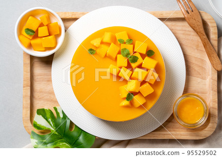 Delicious glazed mango no baked cheese cake with fresh diced mango pulp topping on bright table background. 95529502