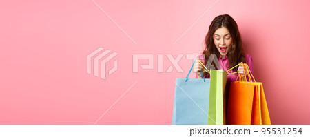 Excited girl open up shopping bags and gasping amazed, checking out gifts for her with happy face, standing against pink background Excited girl open up shopping bags and gasping amazed, checking out gifts for her with happy face, standing against pink background 95531254