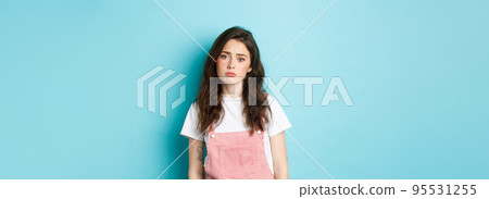 Image of sad and tired young woman feel lonely and upset, sighing, looking indifferent at camera, standing against blue background Image of sad and tired young woman feel lonely and upset, sighing, looking indifferent at camera, standing against blue background 95531255