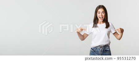 Excited happy brunette girl smiling, pointing fingers at logo, showing banner 95531270