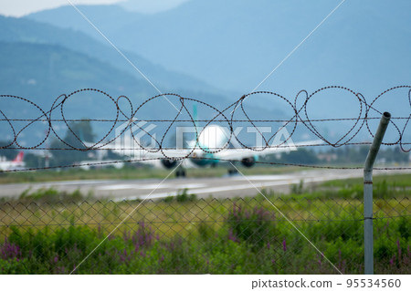 Barbed wire fence of airport against background of landing plane Barbed wire fence of airport against background of landing plane 95534560