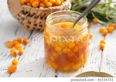Jar of healthy sea buckthorn jam on white white table. Basket of sea buckthorn berries on background. Jar of healthy sea buckthorn jam on white white table. Basket of sea buckthorn berries on background. 95534733