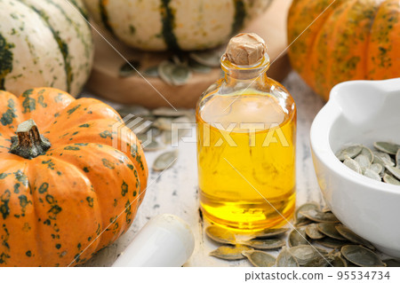 Pumpkin seeds oil bottle, pumpkins and mortar of seeds on wooden kitchen table. Pumpkin seeds oil bottle, pumpkins and mortar of seeds on wooden kitchen table. 95534734