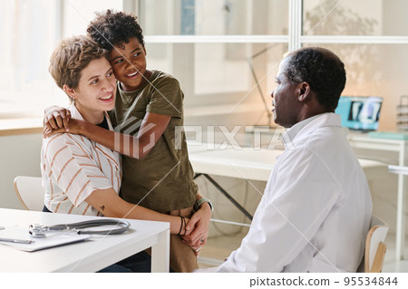 Mom with son smiling while talking to doctor about treatment during their visit at clinic Mom with son smiling while talking to doctor about treatment during their visit at clinic 95534844