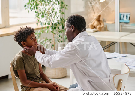 African pediatrician examining sore throat of little patient during medical exam at office African pediatrician examining sore throat of little patient during medical exam at office 95534873