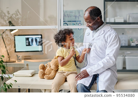 African little boy using stethoscope to listen to heartbeat of doctor while they sitting on couch at hospital 95534880
