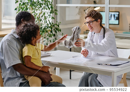 Female doctor showing the toy to little child while they sitting at office during visit at hospital Female doctor showing the toy to little child while they sitting at office during visit at hospital 95534922