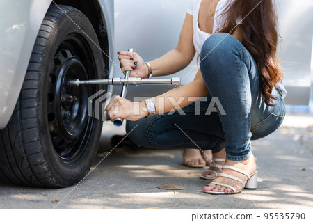 Smart and Attractive Asian woman jacks up her car and uses a wrench to change the wheel on a broken car, uses tools or equipment, tries to solve problems by self, Car Repairing and insurance concept 95535790