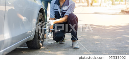 Expertise mechanic man in uniform using force trying to unscrew the wheel bolts nuts and help a woman for changing car wheel on the highway, car service, repair, maintenance concept. Expertise mechanic man in uniform using force trying to unscrew the wheel bolts nuts and help a woman for changing car wheel on the highway, car service, repair, maintenance concept. 95535902