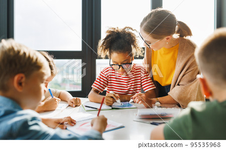 Teacher helping children with schoolwork at school 95535968